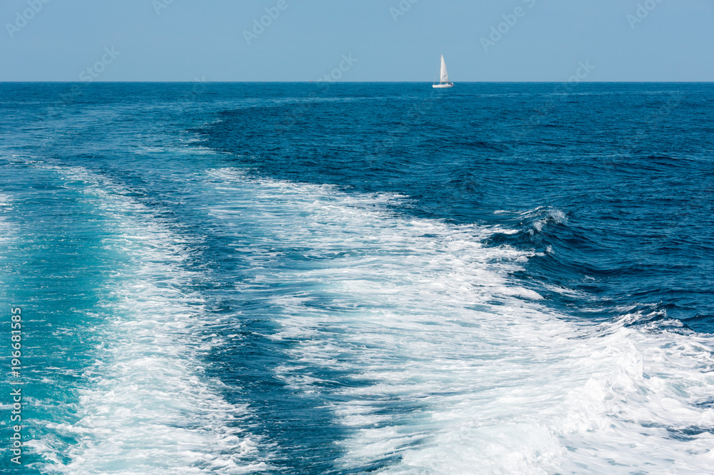 Trace on water surface in the sea and sailing vessel in far