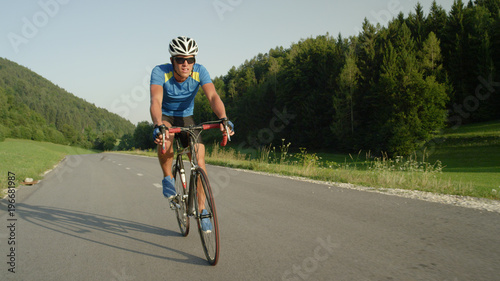 Professional male cyclist cruises down empty asphalt road on a sunny spring day.