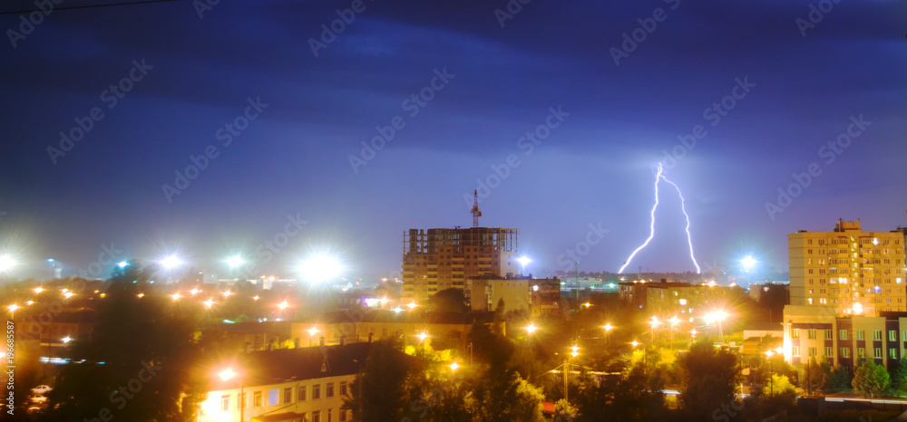 lightning in the night sky over the city. The flash of lightning illuminates the city and the construction site with a multi-storey building