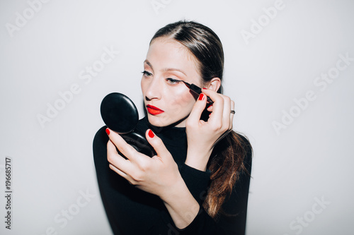 Young woman holding hand mirror and applying eyeliner