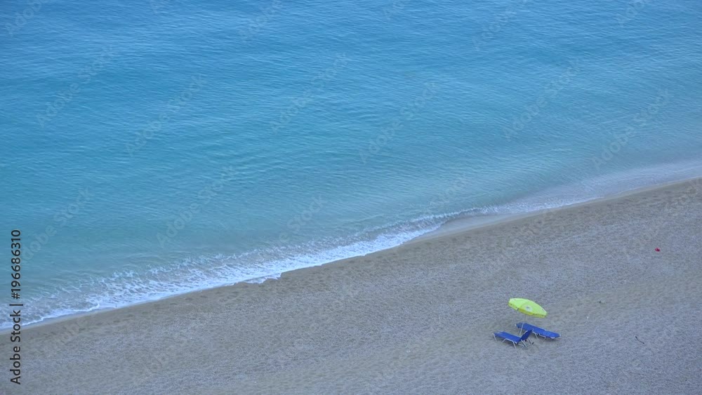 One umbrella with two sunbed lounge chairs on beach turquoise wave moving 4K One umbrella with two sunbed lounge chairs on beach turquoise wave moving 4K