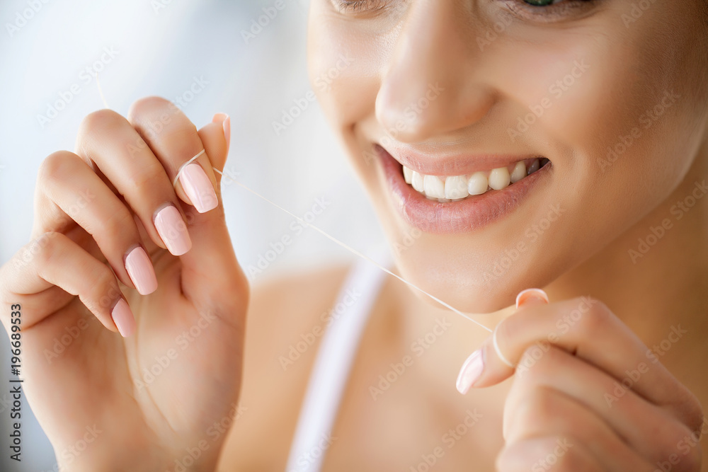 Close up of female face with perfect smile. Girl is cleaning teeth by special thread Close up of female face with perfect smile. Girl is cleaning teeth by special thread