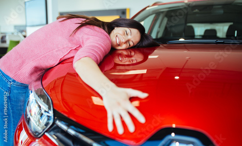 Happy beautiful young woman buying a new car at the car showroom.
