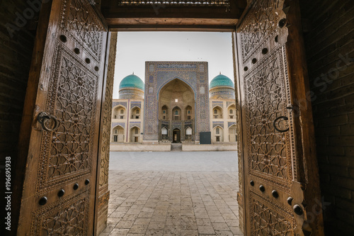 Mir-Arab-Madrasa seen through beautiful ornate wooden door at sunrise, buxoro, uzbekistan