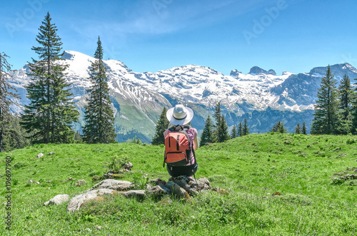 Swiss Alps. A woman in a white hat is sitting on a green meadow, admiring the mountain scenery. Engelberg Resort