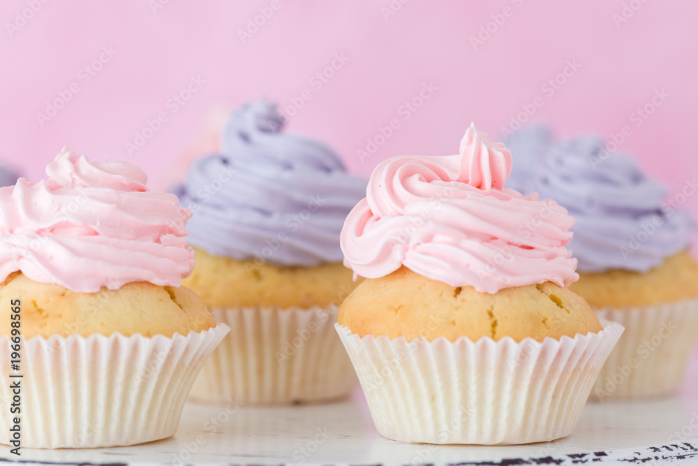 Cupcakes with pink and violet buttercream standing on pastel pink background. Cupcakes with pink and violet buttercream standing on pastel pink background.