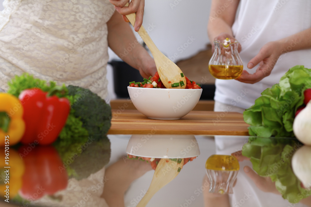 Closeup of human hands cooking in kitchen. Mother and daughter or two female friends mixing salad of vegetables. Healthy meal, vegetarian food and lifestyle concepts