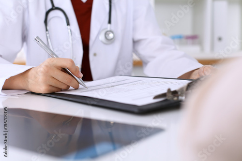 Close up of a female doctor filling up  an application form while consulting patient © rogerphoto