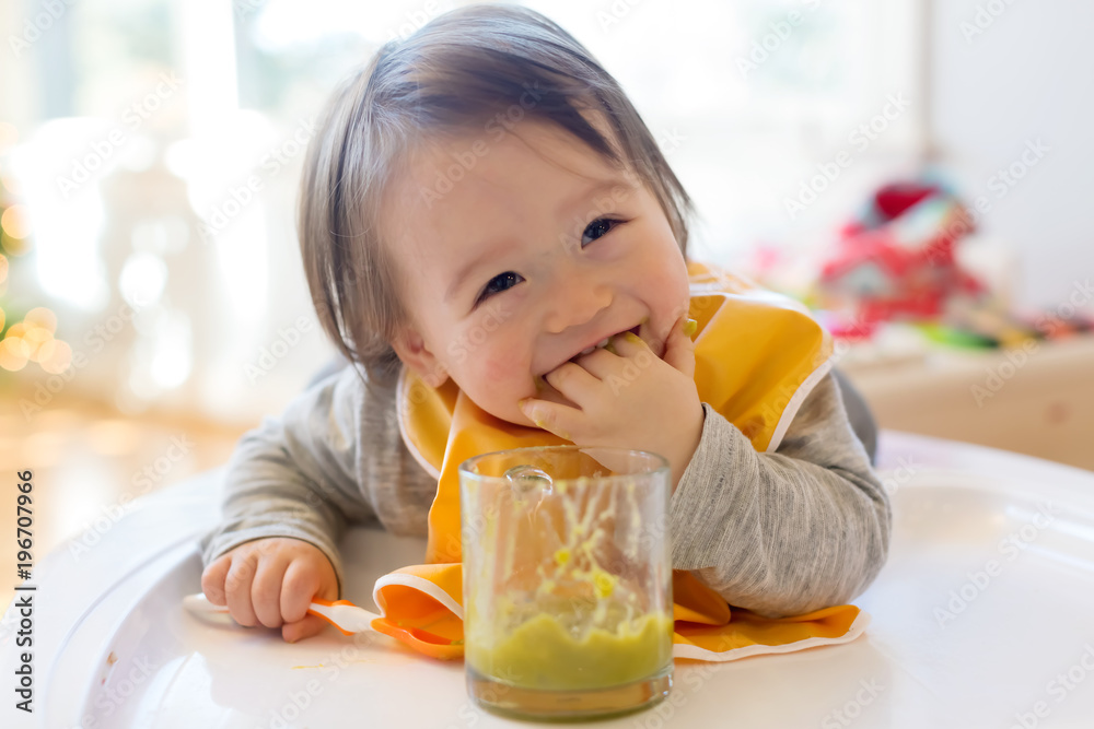 Happy little baby boy eating food in his house