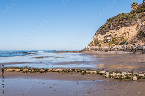 An empty Swami's Beach at low tide, with view of cliff and rocky reef covered in algae.