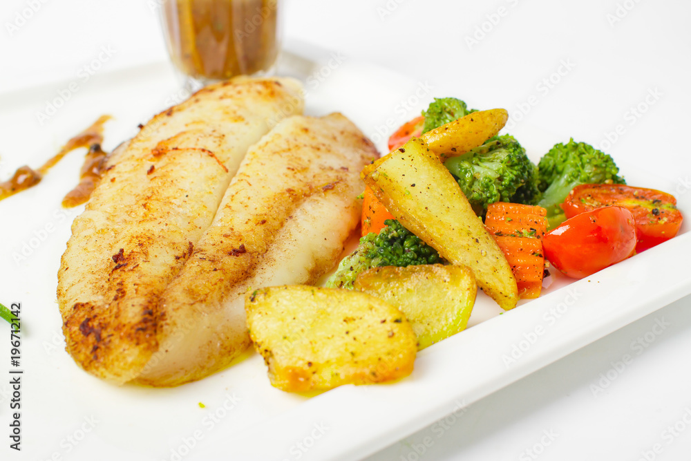 Grilled fish fillets steak served with mix vegetable, potatoes and a glass of black pepper gravy sauce on white background Grilled fish fillets steak served with mix vegetable, potatoes and a glass of black pepper gravy sauce on white background