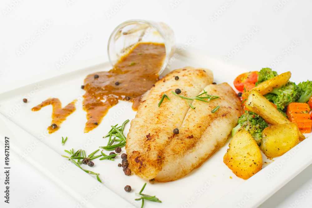 Grilled fish fillets steak served with mix vegetable, potatoes and a glass of black pepper gravy sauce on white background