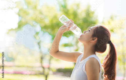 Young beautiful woman  drinking water at summer green park.