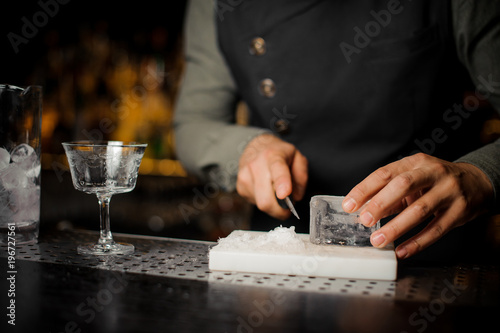 Barman preparing a piece of ice for making cocktail