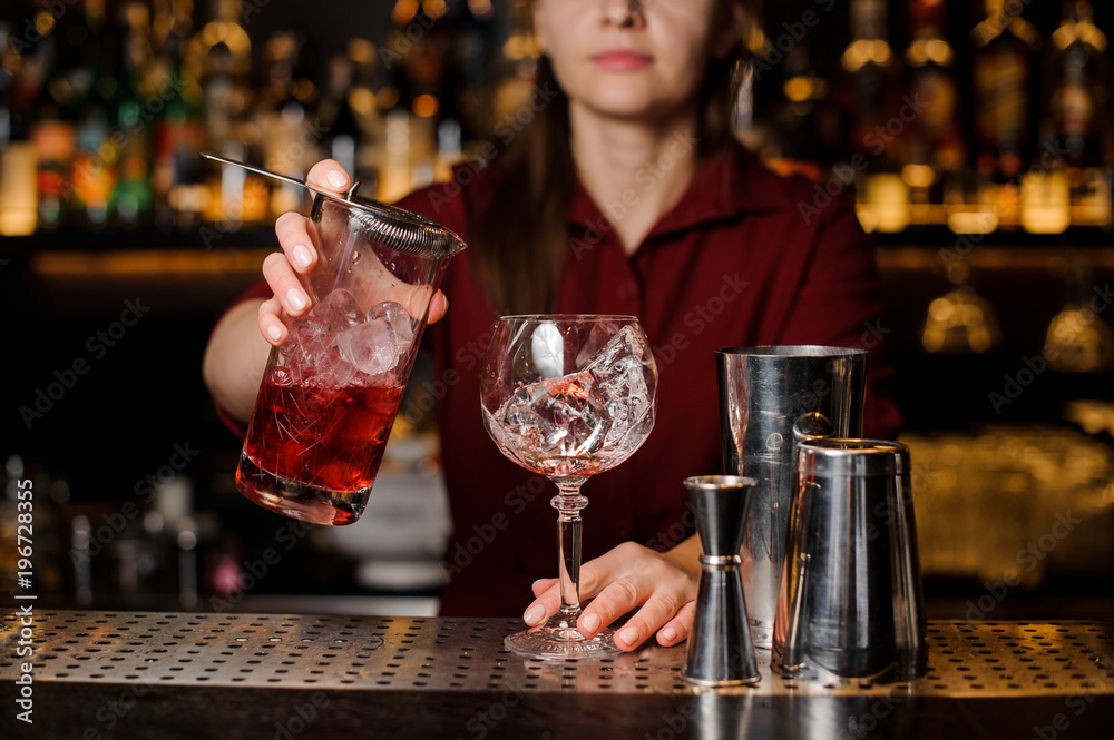 Female barman pouring sweet red alcoholic drink into a glass