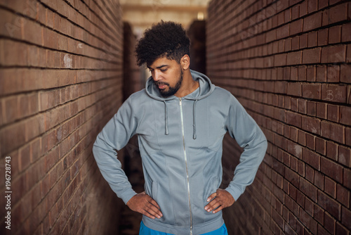 Portrait of focused motivated afro-american young handsome sportive man standing inside of the abandoned place in the middle of two walls and thinking. photo