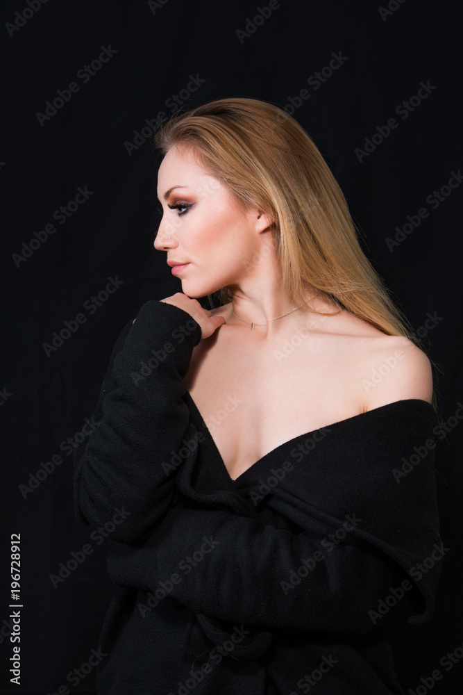 Naklejka premium Profile of sexy lady with glamour makeup and long blonde hair in long coat posing in studio, dark background. Elegant woman. Erotic noir concept.