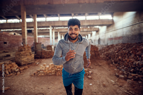 Portrait of happy motivated focused afro-american young sportive man training inside of the abandoned hangar place with earphones. photo