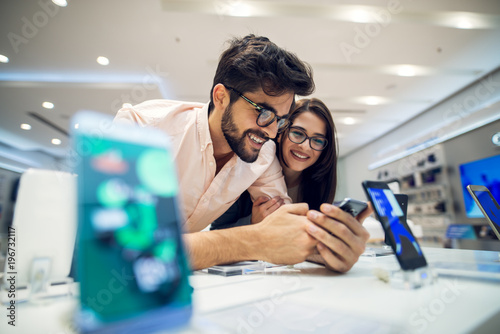 Close up focus view of a cheerful charming happy young student love couple choosing a new mobile in a tech store.