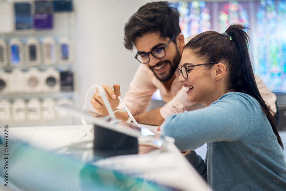 Close up side view of excited charming happy young student love couple smiling to a new tablet in a tech store.
