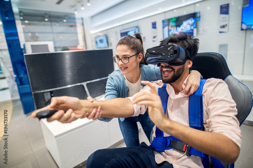 Young cute playful love couple having fun with VR goggles in the tech store. Young cute playful love couple having fun with VR goggles in the tech store.