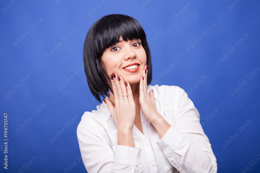 Beautiful surprised woman with her hands on the face on blue background in studio photo Beautiful surprised woman with her hands on the face on blue background in studio photo