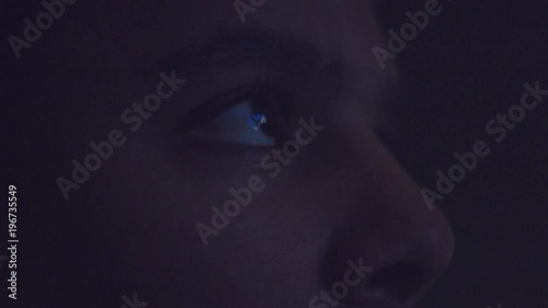 upset boring mixed race man watching tv in darkness with different color light from tv on face. Eyes closeup