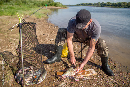 a fisherman is cutting fish on the river bank
