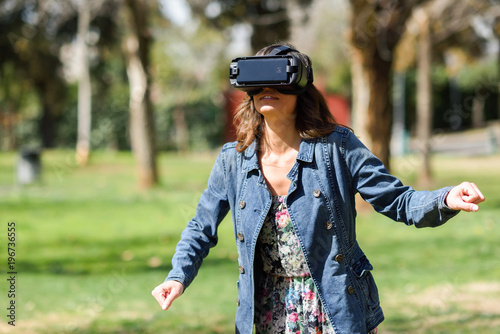 Woman looking in VR glasses and gesturing with his hands outdoors
