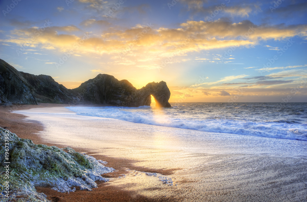Fototapeta premium Landscape image of sunrise shining through the arch of Durdle Door on the Jurassic Coast