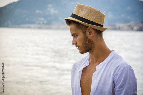 Handsome Young Man in Trendy Attire, on a Beach in a Sunny Summer Day, Wearing a White Shirt and Straw Hat © theartofphoto