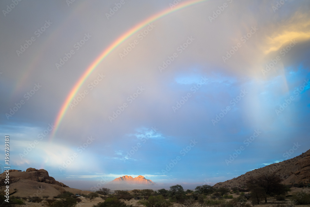 A double rainbow and approaching rain storm with clouds in the sky above the plains of Namibia with a mountain on the horizon
