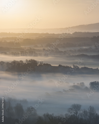 Stunning foggy English rural landscape at sunrise in Winter with layers rolling through the fields