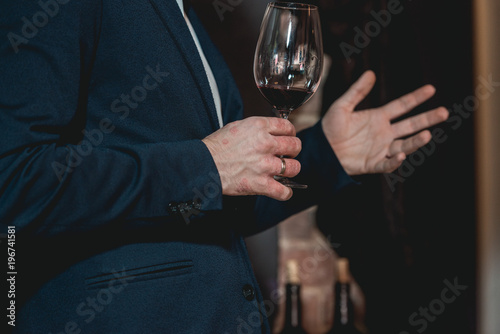 man in a blue suit with a skin disease holds glass of red wine. people consider the color of the wine and try how it smells in different glasses