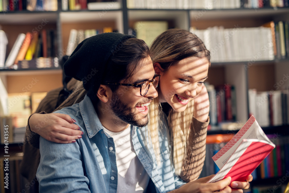 Close up of charming satisfied cheerful young student love couple reading a book together in the school library. Close up of charming satisfied cheerful young student love couple reading a book together in the school library.