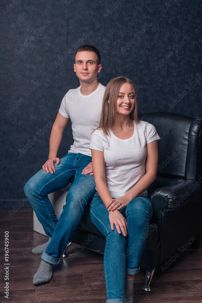 Beautiful couple girl and guy sitting in a chair in white T-shirts and jeans Beautiful couple girl and guy sitting in a chair in white T-shirts and jeans