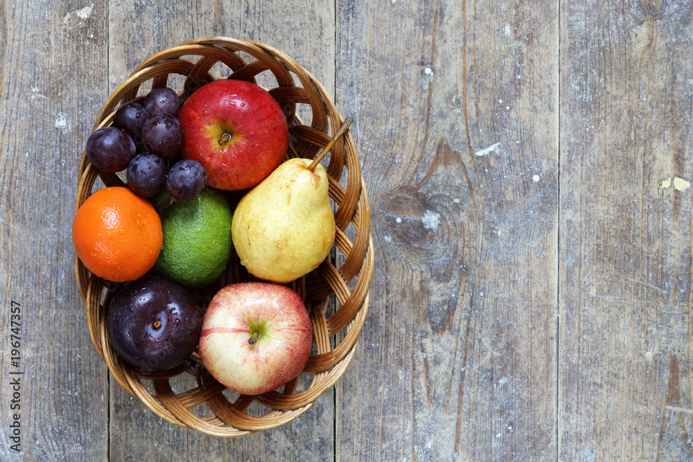 Mixed fruits of apples, lime, lemon, pears and plums in wicker bowl on wood table with copy space right Mixed fruits of apples, lime, lemon, pears and plums in wicker bowl on wood table with copy space right