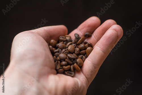 Hand holding coffee beans on dark background. Place for text or design