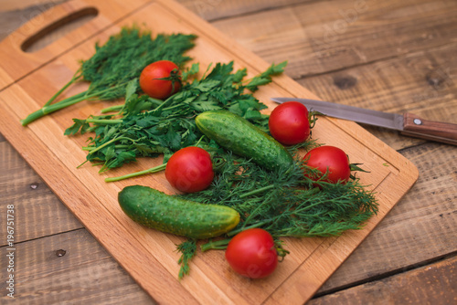 Cherry tomatoes, cucumbers, dill and parsley on wooden board on table with knife closeup. Healthy food concept.