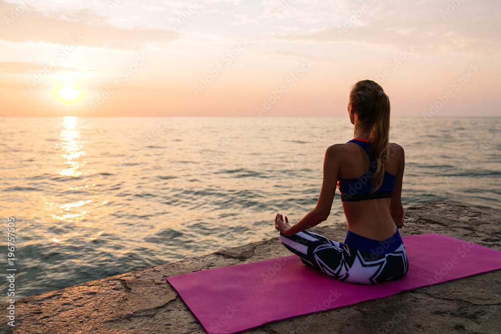 Sportive girl sitting in lotus position on sunset, near the sea