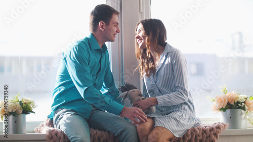 Foto Young and attractive guy and girl sitting on the windowsill and kissing, guy giv