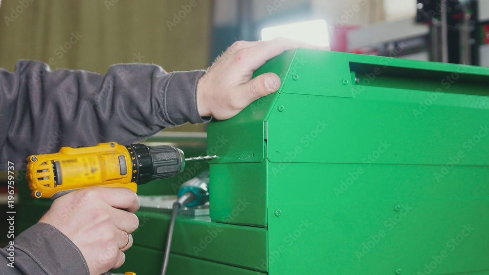 Worker man using an electric hand drill - making hole in green metal machine Worker man using an electric hand drill - making hole in green metal machine