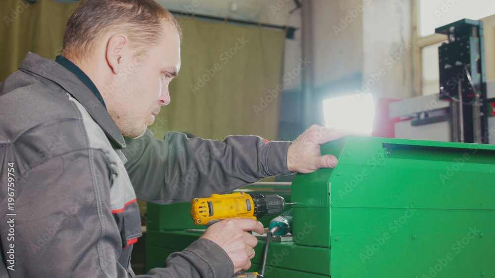 Worker man using an electric hand drill - making hole in green metal machine Worker man using an electric hand drill - making hole in green metal machine