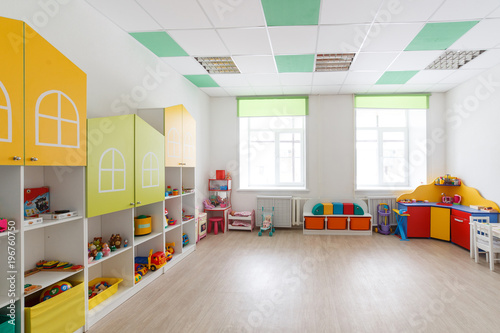 Spacious white game room in the kindergarten with toys, two large windows and tables for classes. photo