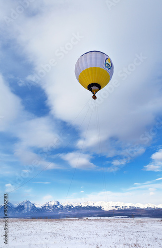 Hot air balloon with tourists in a basket against a blue sky with clouds. The shell of the ball depicts the official coat of arms of the Republic of Buryatia (not an object of copyright)