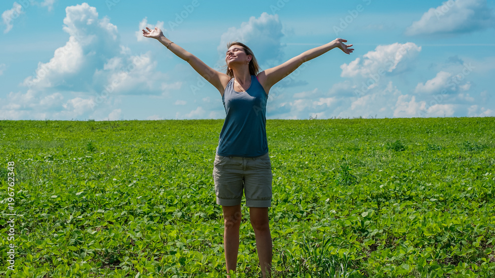 Pretty young happy blondy girl open up hands in the field on sunny day, blue sky background