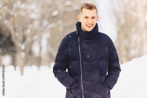 A guy with light short hair in a winter jacket poses to the camera
