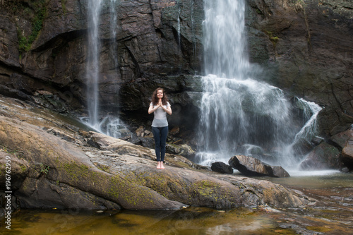 Young woman in namaste pose with waterfall behind