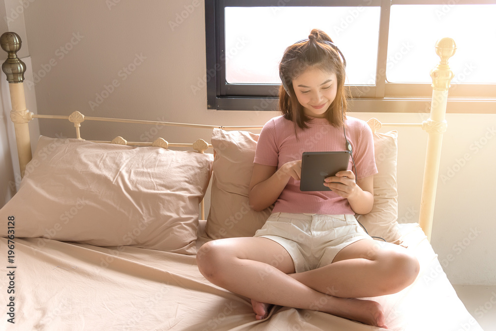 Happy young woman sitting in her bedroom, hand holding iPad online connect to her friend, technology concept. Happy young woman sitting in her bedroom, hand holding iPad online connect to her friend, technology concept.