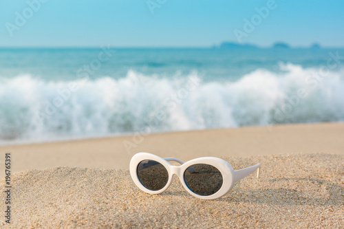 Fototapeta Naklejka Na Ścianę i Meble -  white plastic fashion sunglasses on sand dune near the beach with sea wave and bubbles at back